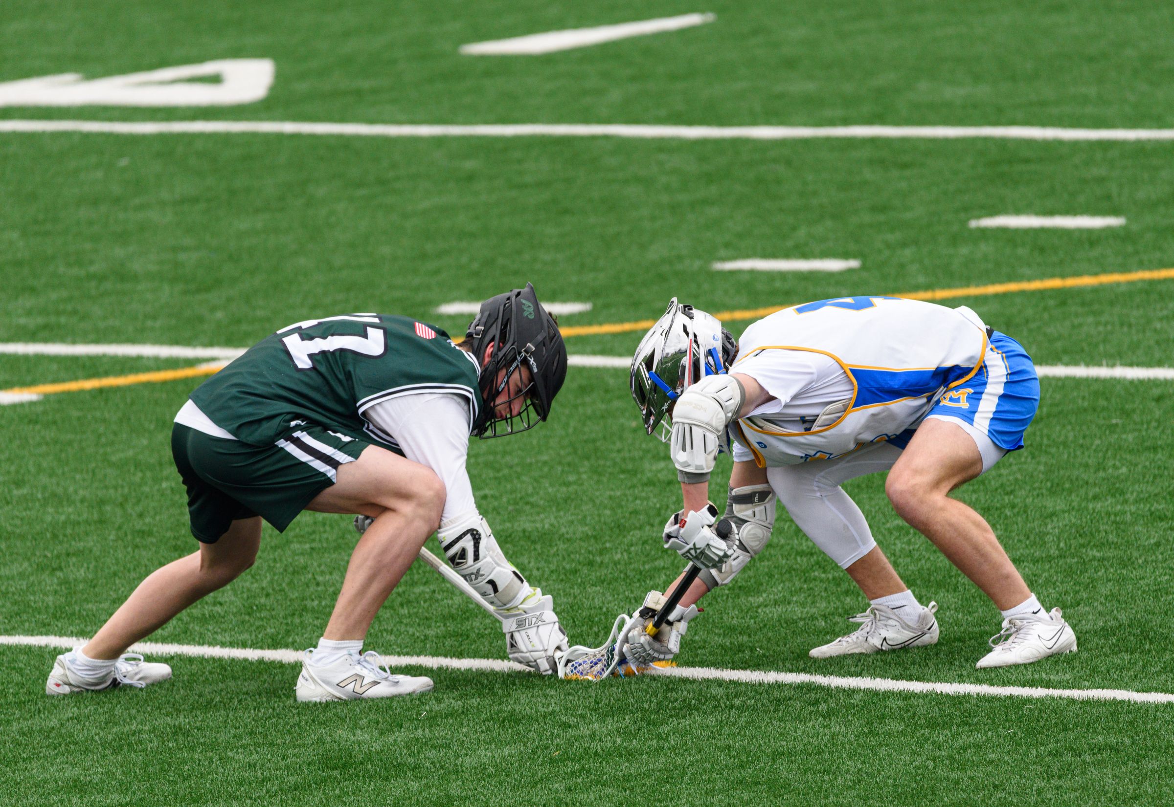 Two lacrosse players facing off on a turf field